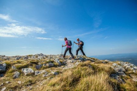 couple-hiking-nanos-plateau-slovenia-against-blue-sky